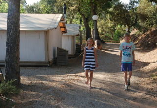 Dos niños caminan por el sendero frente a la tienda SunLodge Safari en Camping Leï Suves, Francia.