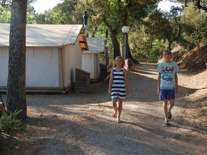 Dos niños caminan por el sendero frente a la tienda SunLodge Safari en Camping Leï Suves, Francia.