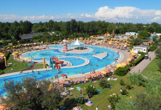 Vista aérea de un parque acuático concurrido en un lodge, con piscinas, toboganes y muchas sombrillas.
