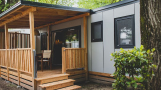 Exterior view of SunLodge Babul, a modern lodge with a wooden deck and surrounded by lush greenery.