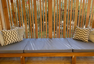Banco exterior con cojines grises y estampados, detrás de listones de madera en SunLodge Babul.