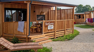 Houten SunLodge BigLeaf met overdekt terras, ligstoel en pad in een rustige, natuurlijke omgeving.
