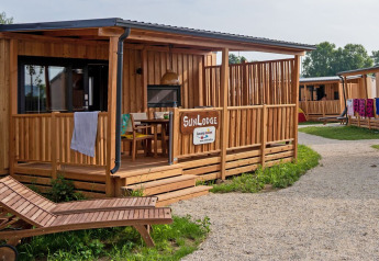 Houten SunLodge BigLeaf met overdekte veranda, ligstoel en grindpad in een rustige, groene omgeving.