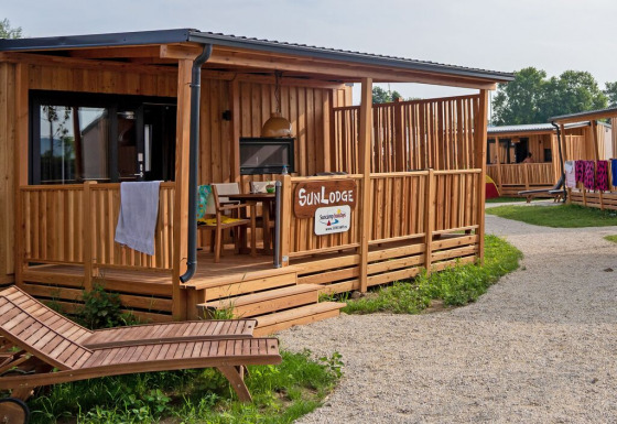 Cabane en bois SunLodge BigLeaf avec terrasse ombragée, transat et sentier de gravier dans un cadre paisible.