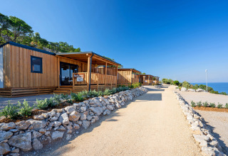 Cabañas de madera modernas alineadas junto a un sendero de grava con vista al mar y cielo despejado.