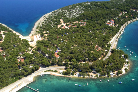 Vista aérea de un lodge costero rodeado de bosque frondoso y agua turquesa, con barcos en la orilla.