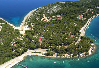 Aerial view of a coastal lodge surrounded by dense forest and clear turquoise water with boats nearby.