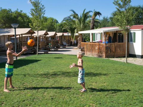 Twee kinderen spelen met een bal op het gras voor SunLodge Maple hutten in Camping Vilanova Park, Spanje.