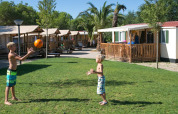 Twee kinderen spelen met een bal op het gras voor SunLodge Maple hutten in Camping Vilanova Park, Spanje.