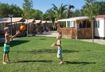 Due bambini giocano con una palla sul prato davanti ai lodge SunLodge Maple al Camping Vilanova Park, Spagna.