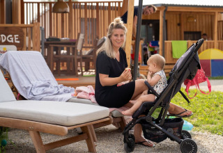 Maman assise sur une chaise longue près d'une poussette avec bébé devant SunLodge BigLeaf en Italie.