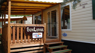 Vista exterior de SunLodge Redwood, con porche de madera, toldo amarillo y letrero de entrada.