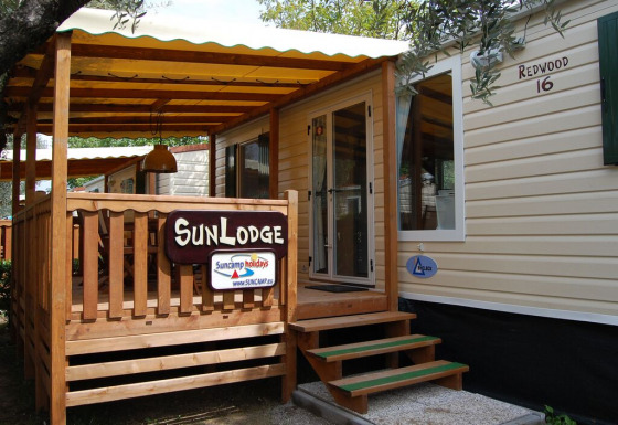 Vista exterior de SunLodge Redwood, con porche de madera, toldo amarillo y letrero de entrada.