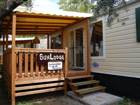 Udendørsbillede af SunLodge Redwood-hytte med træterrasse, skilte og grønne omgivelser.
