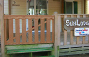 Entrada de SunLodge Redwood en Camping Cisano/San Vito, Italia, con porche de madera y letreros visibles.
