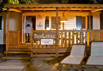 Vista serale di SunLodge Redwood al Camping Cisano/San Vito in Italia con veranda illuminata e sedie.