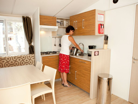 Vrouw maakt thee in de kitchenette van SunLodge Redwood Premium op Camping Cisano/San Vito in Italië.