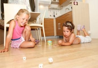 Dos niños juegan con dados en el suelo de una cocina moderna en SunLodge Redwood Premium, Camping Cisano/San Vito, Italia.