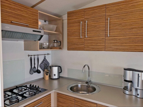 Cocina moderna en un lodge con estufa de gas, fregadero, hervidor, cafetera y armarios de madera.