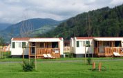 Solrige mobilhytter ved SunLodge Maple på Camping Bella Austria omgivet af grønne bakker og bjerge.