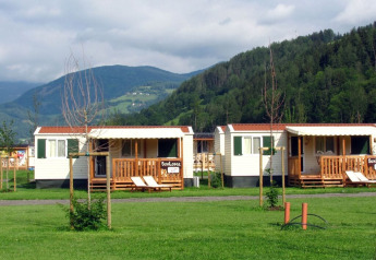 Solrige mobilhytter ved SunLodge Maple på Camping Bella Austria omgivet af grønne bakker og bjerge.