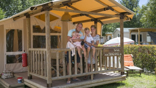 Family enjoying vacation on the porch of a SunLodge Safari at Camping Pra'delle Torri in Italy.