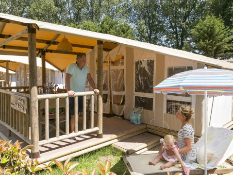 Familia disfrutando al aire libre frente a SunLodge Safari en Camping Pra'delle Torri, Italia, con sol y relax.