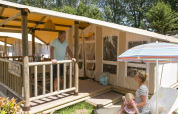 Familia disfrutando al aire libre frente a SunLodge Safari en Camping Pra'delle Torri, Italia, con sol y relax.