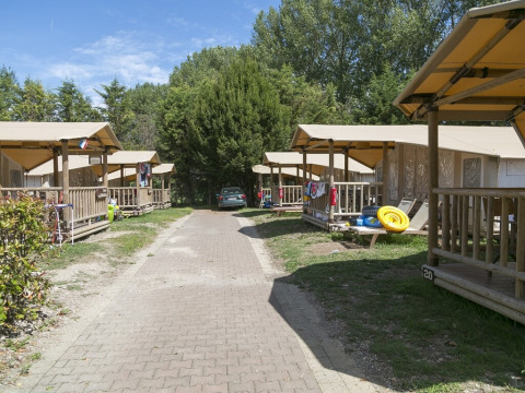 Tiendas SunLodge Safari en Camping Pra'delle Torri, Italia, alineadas en un sendero con vegetación.