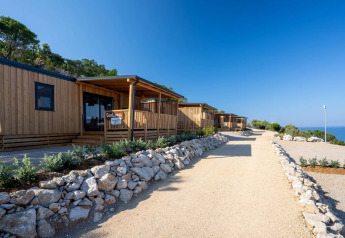 Houten SunLodge BigLeaf lodges langs een grindpad, omgeven door stenen, groen en uitzicht op zee.