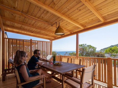 Pareja relajándose en la terraza de madera de SunLodge BigLeaf en Camping Village Poljana, Croacia, con vista al mar.