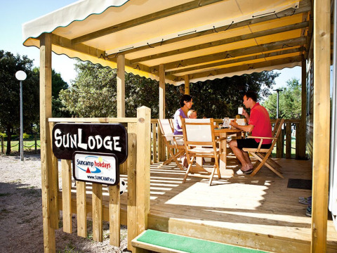 Familia desayunando en la terraza de madera bajo toldo en SunLodge Aspen, Camping Village Poljana, Croacia.