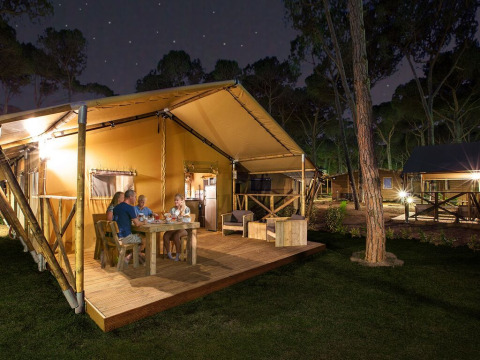 Familia cenando en la terraza de madera de SunLodge Bintulu en Camping Village Poljana, Croacia, de noche.