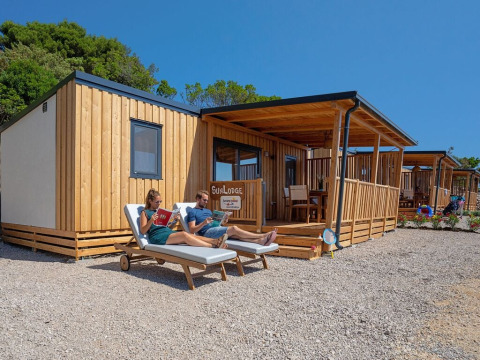 Dos personas se relajan en tumbonas frente a una cabaña de madera SunLodge Catalpa en un día soleado.