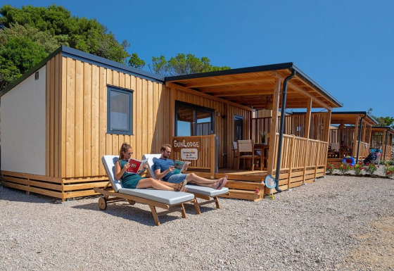 Dos personas se relajan en tumbonas frente a una cabaña de madera SunLodge Catalpa en un día soleado.