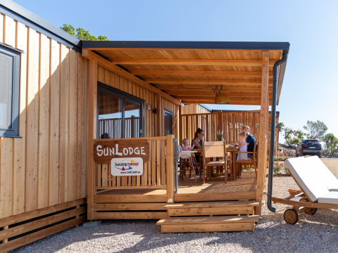 Gezin op het houten terras bij SunLodge Catalpa op Camping Village Poljana, Kroatië, met zonnig weer.
