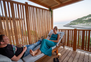 Dos personas se relajan en una terraza de madera con vistas al mar en SunLodge Catalpa, Camping Village Poljana, Croacia.