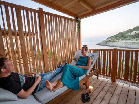 Dos personas se relajan en una terraza de madera con vistas al mar en SunLodge Catalpa, Camping Village Poljana, Croacia.