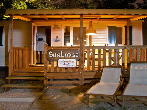 Vista nocturna de SunLodge Redwood en Camping Village Poljana, Croacia, con porche y tumbonas iluminados.