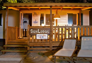 Vista nocturna de SunLodge Redwood en Camping Village Poljana, Croacia, con porche y tumbonas iluminados.