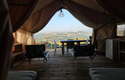 Blick aus einem Safari-Zelt bei Agricola La Casetta, Italien, mit Terrasse und Hügelpanorama im Hintergrund.