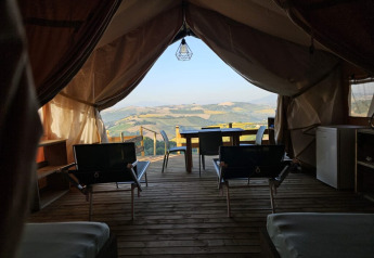 Blick aus einem Safari-Zelt bei Agricola La Casetta, Italien, mit Terrasse und Hügelpanorama im Hintergrund.