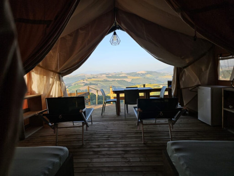 Vista dall'interno di una tenda safari all'Agricola La Casetta, Italia, con terrazza e colline sullo sfondo.