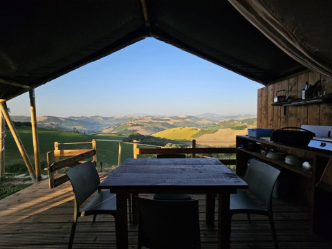 Área de comedor exterior en tienda safari con vistas a colinas en un alojamiento glamping pintoresco.