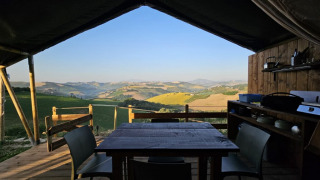 Área de comedor exterior en tienda safari con vistas a colinas en un alojamiento glamping pintoresco.