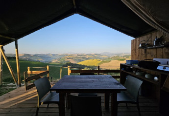 Essbereich im Safarizelt mit Blick auf grüne Hügel, aufgenommen bei einer Glamping-Unterkunft.
