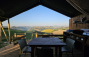 Área de comedor exterior en tienda safari con vistas a colinas en un alojamiento glamping pintoresco.