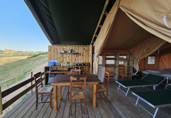 Safari-Zelt-Glamping-Unterkunft mit Holzterrasse, Esstisch, Liegestühlen und Blick auf die Natur.