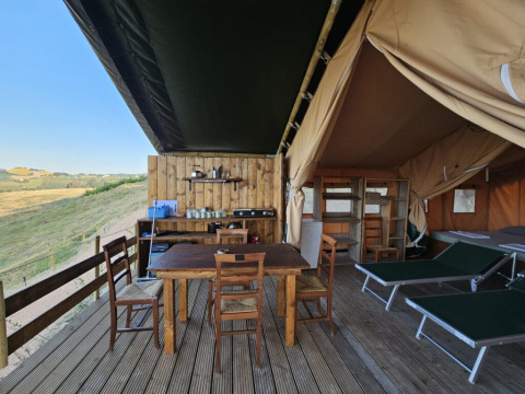 Alojamiento de glamping en tienda safari con terraza de madera, mesa, tumbonas y vista a la naturaleza.