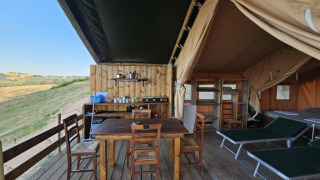 Safari tent glamping accommodatie met houten terras, eettafel, ligstoelen en uitzicht op de natuur.